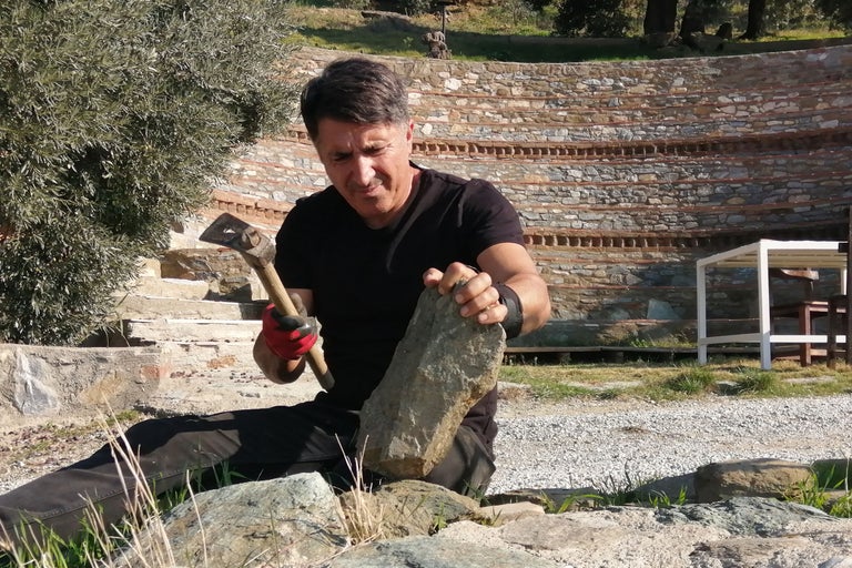 Un homme travaille la pierre avec un marteau à l'extérieur.