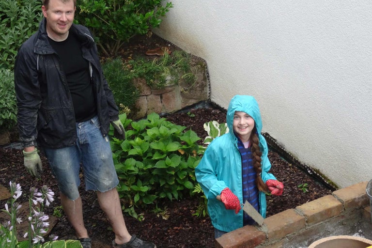 Gartenarbeitsszene mit einem Mann und einem Mädchen beim Bau einer Mauer mit Ziegeln und Mörtel inmitten von Pflanzen