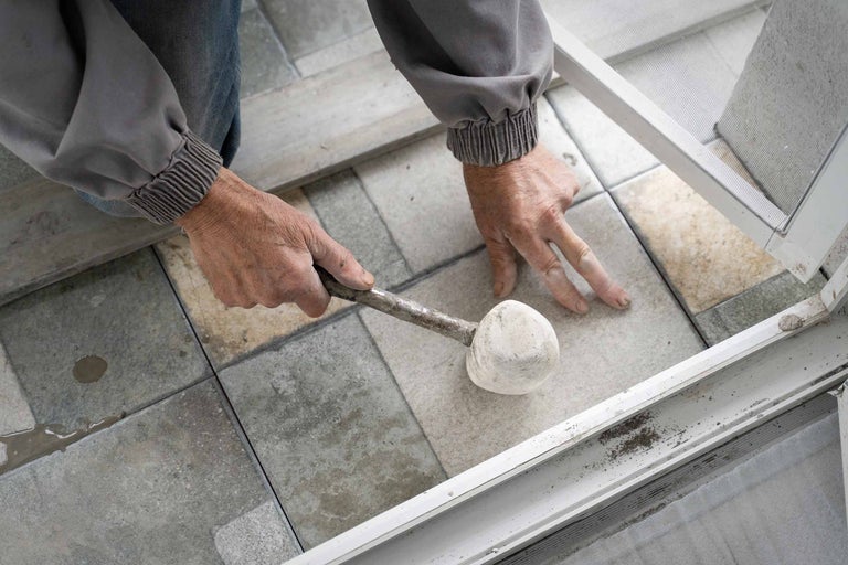 Un artisan répare une moustiquaire avec un maillet en caoutchouc.