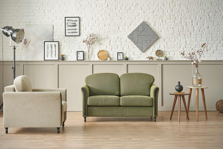 Salon avec un canapé vert, un fauteuil et des décorations devant un mur de briques blanc