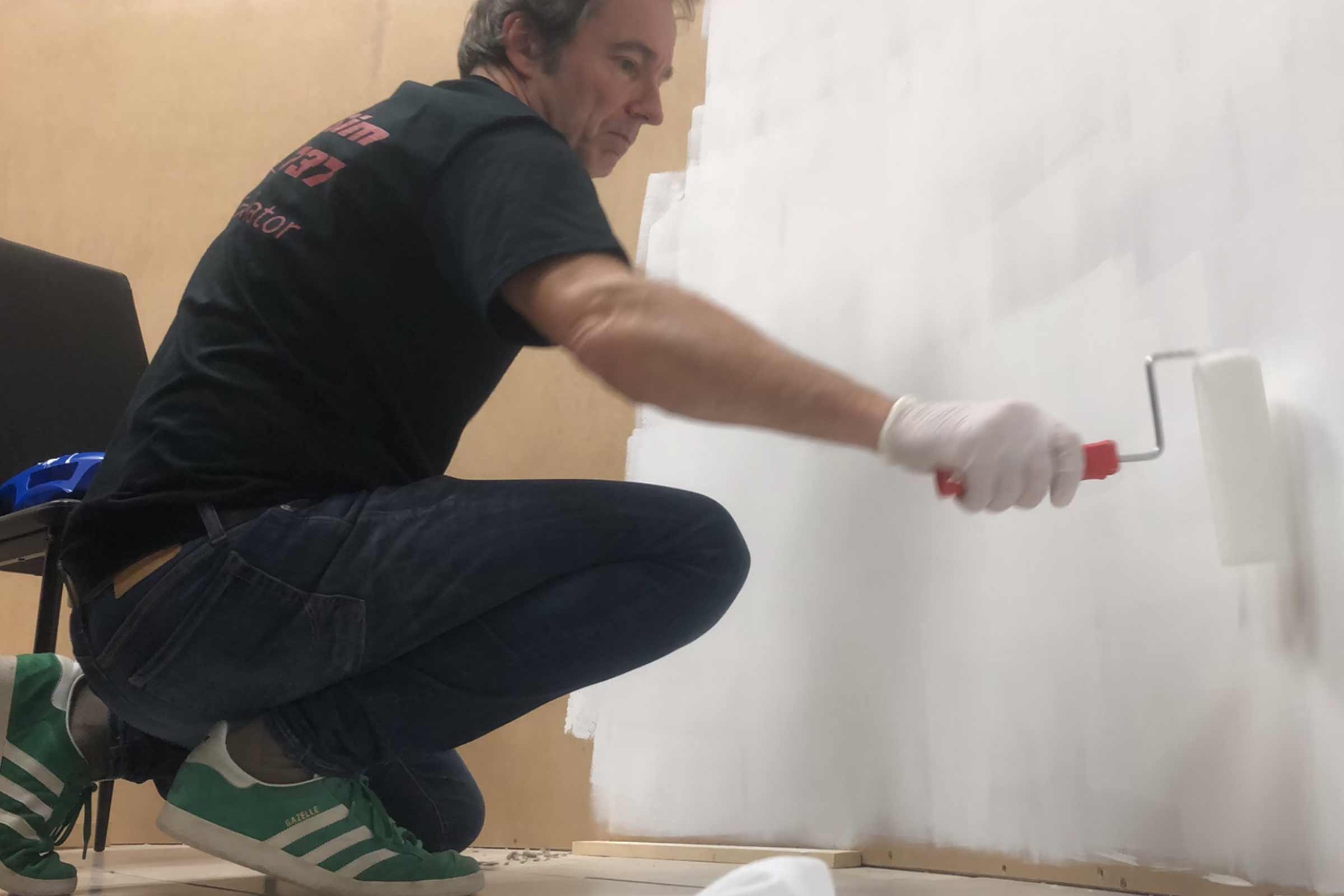 Un homme peint un mur avec un rouleau à peinture.