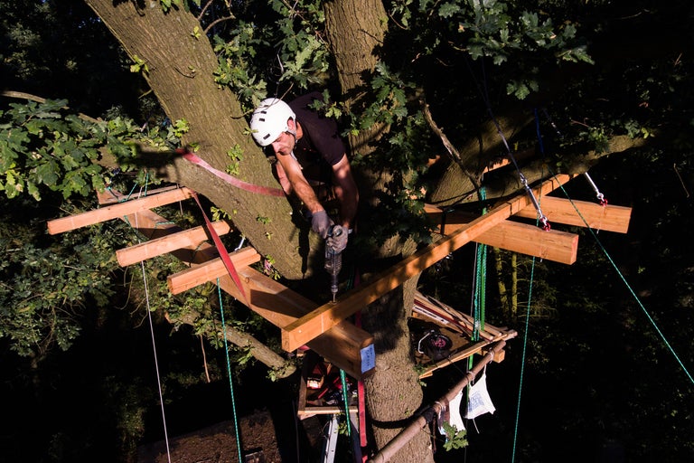 Mann mit Bohrmaschine beim Bau eines Baumhauses