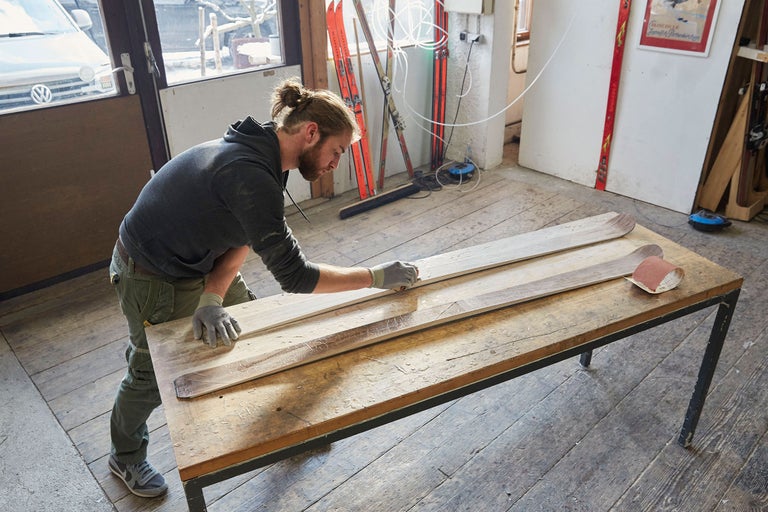 Un homme ponce des skis en bois sur un établi dans un atelier