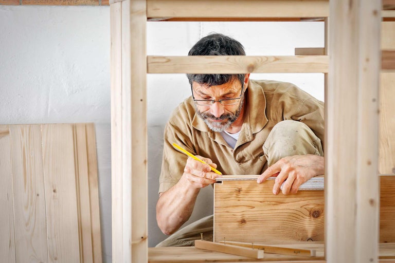 Un homme mesure une planche de bois avec un mètre et un crayon dans un atelier.