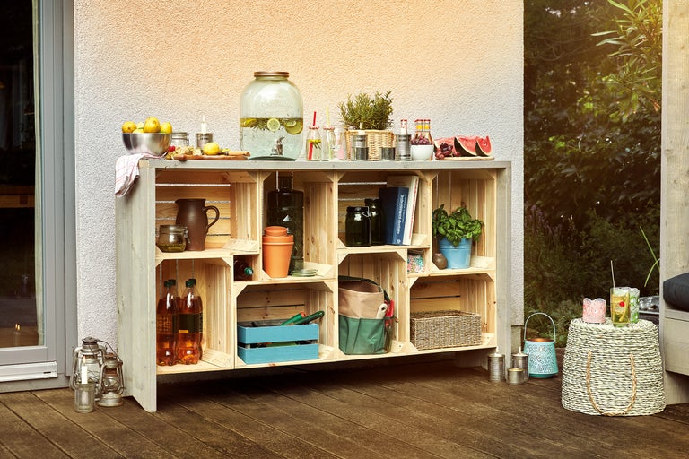Aussenszene mit einem Regal aus Holzkisten, dekoriert mit Getränken, Obst und Pflanzen