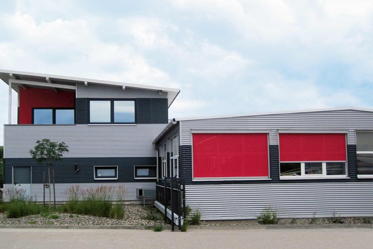 Gebäude mit rotem Sonnenschutzsystem vor den Fenstern.