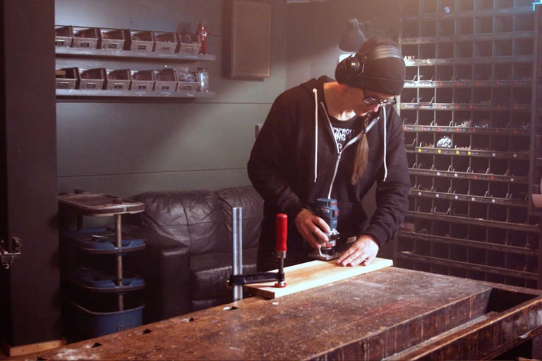 Une personne travaille avec une défonceuse sur une pièce de bois sur un établi dans un atelier.