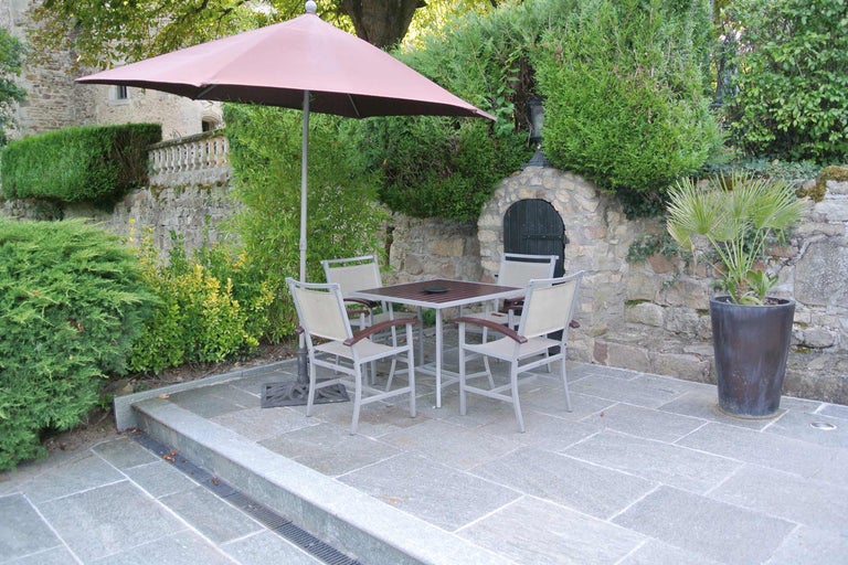 Table de jardin carrée avec quatre chaises et parasol sur une terrasse pavée