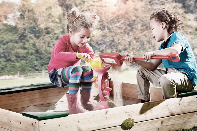 Zwei Kinder spielen mit Sandspielzeug in einem Sandkasten