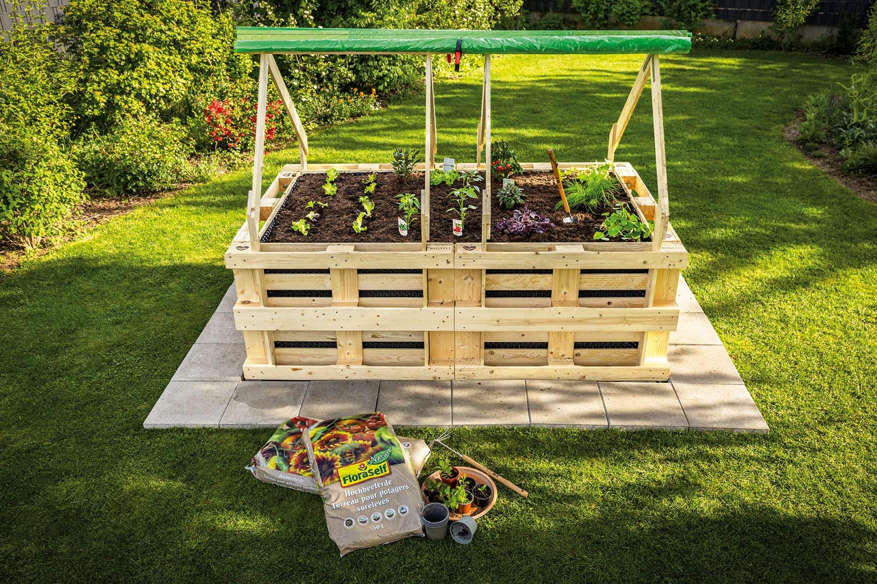 Hochbeet aus Holz mit Pflanzen und Gemüse im Garten, im Vordergrund Blumenerde.