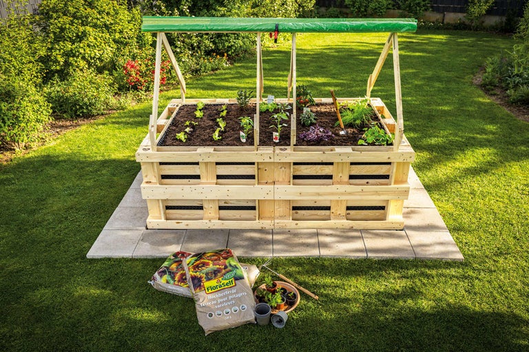 Jardinière surélevée en bois avec plantes et légumes dans le jardin, terreau au premier plan.