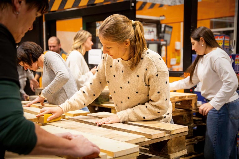 Plusieurs personnes travaillent des palettes en bois avec du papier de verre.
