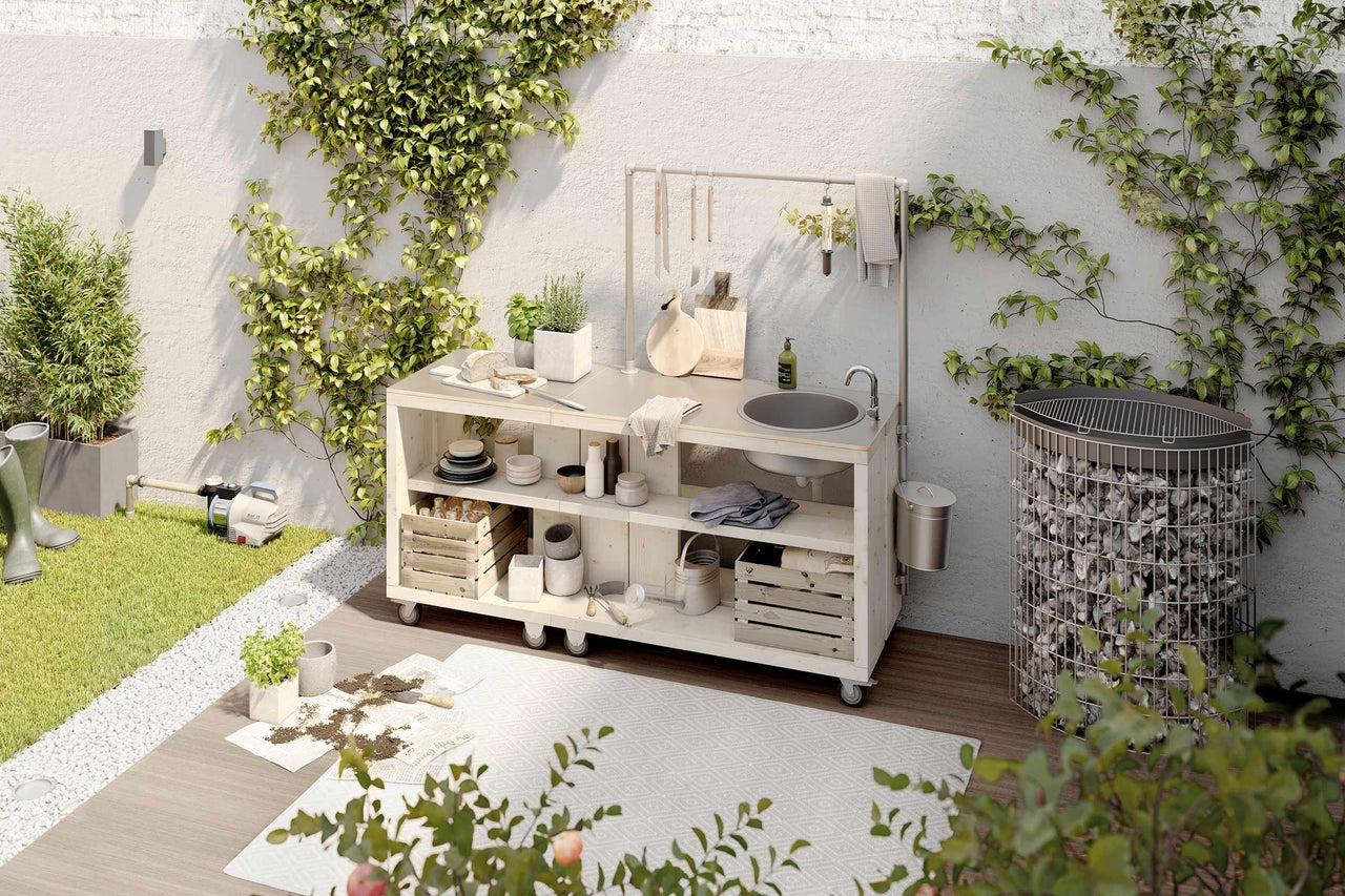 Cuisine extérieure avec évier, barbecue et outils de jardin dans un espace extérieur verdoyant.
