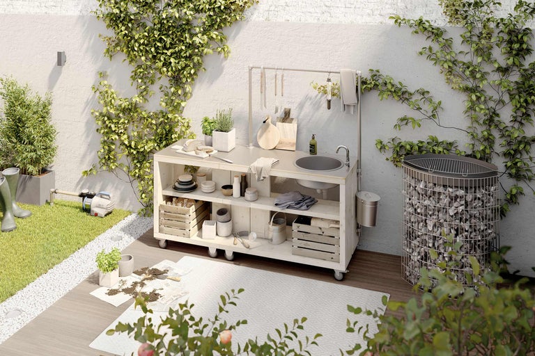 Aussenküche mit Spüle, Grill und Gartengeräten in einem begrünten Aussenbereich.