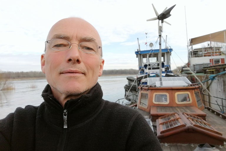 Homme devant une péniche avec panneaux solaires et éolienne