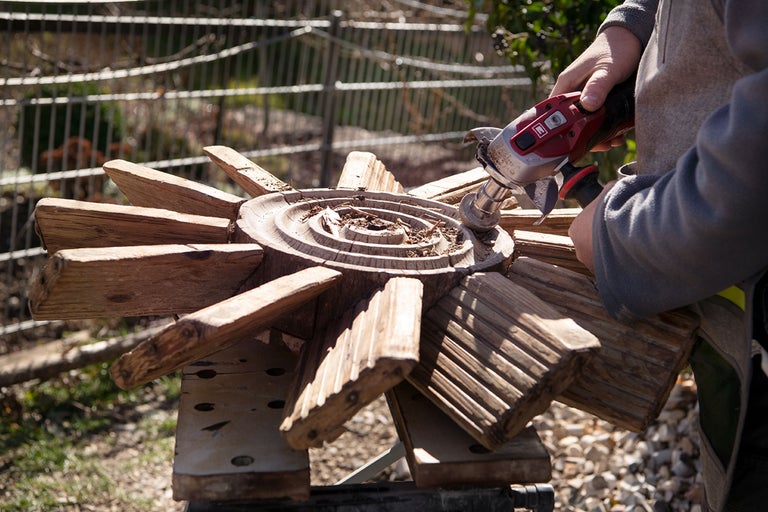 Une personne nettoie une éolienne en bois avec une brosse métallique.
