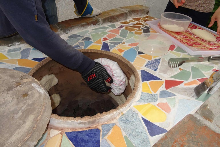 Person legt Brot in einen Lehmofen mit Mosaikfliesen