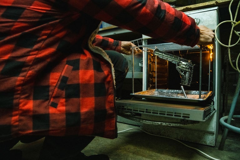 Personne en chemise rouge et noire plaçant un objet métallique dans un four.