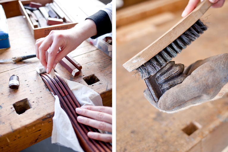 Auf dem Bild sind Holzarbeiten auf einer Werkbank zu sehen. Eine Person reinigt Holzstäbe mit einem Tuch, während eine andere Person eine Metallbürste benutzt, um ein Werkstück zu reinigen. Auf der Werkbank liegen verschiedene Werkzeuge.