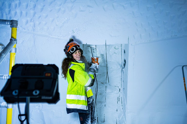 Femme portant un casque et des lunettes de protection travaillant avec une scie électrique dans une pièce aux murs de glace