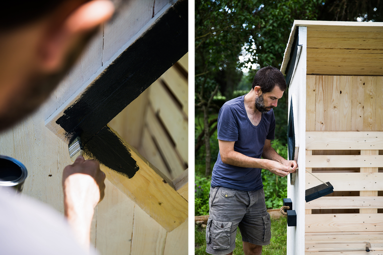 Un homme peint une construction en bois avec de la peinture noire et fixe un verrou.