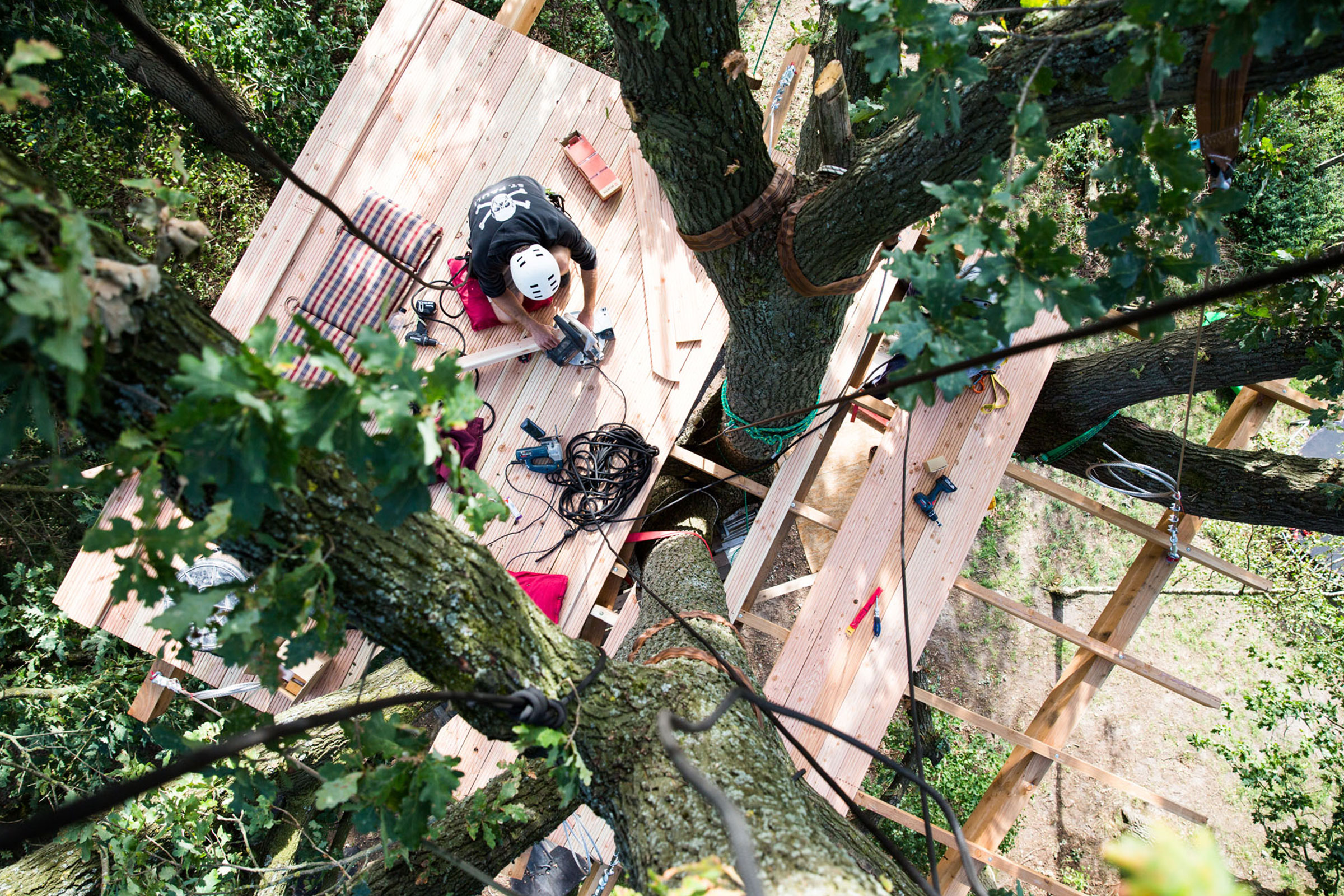 Baumhausbau mit einer Person auf einer Holzplattform in den Baumwipfeln.
