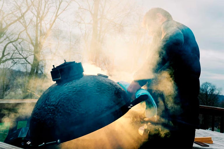 Un homme nettoie un barbecue en céramique à l'extérieur avec une brosse de barbecue