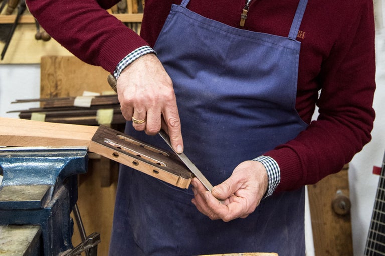 Ein Handwerker bearbeitet einen Gitarrenhals mit einer Feile in einer Werkstatt.