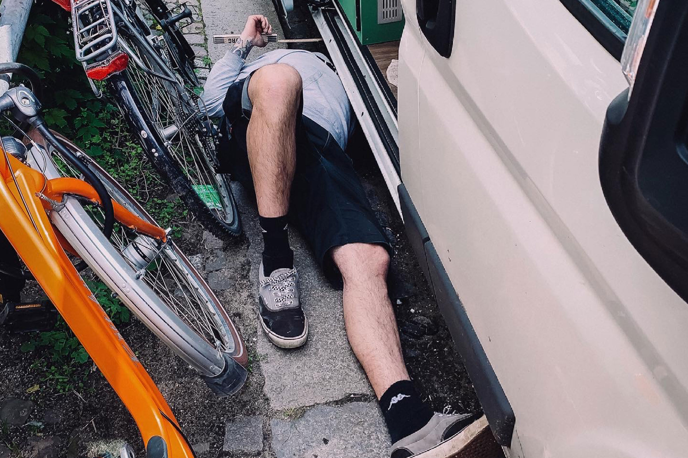 Une personne est allongée sous un véhicule, à côté de vélos.