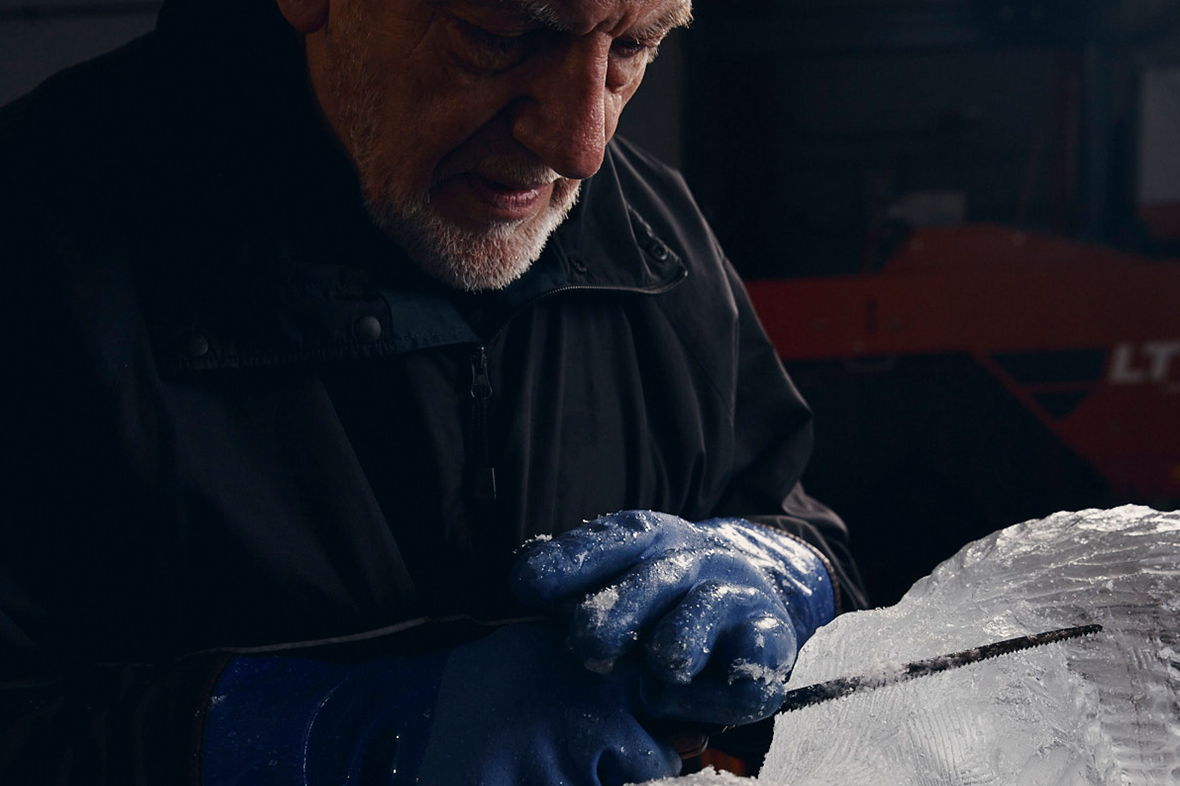 Ein Mann schnitzt eine Eisskulptur mit einer Säge und Handschuhen.