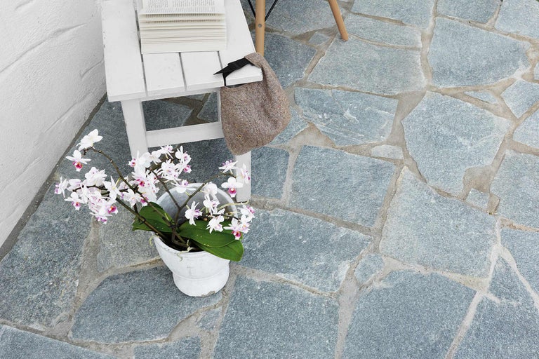 Terrasse avec dalles en pierre naturelle, décorée avec table, livres, sac et plante en pot