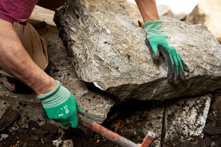 Person setzt einen grossen Stein mit einem Werkzeug und Handschuhen.