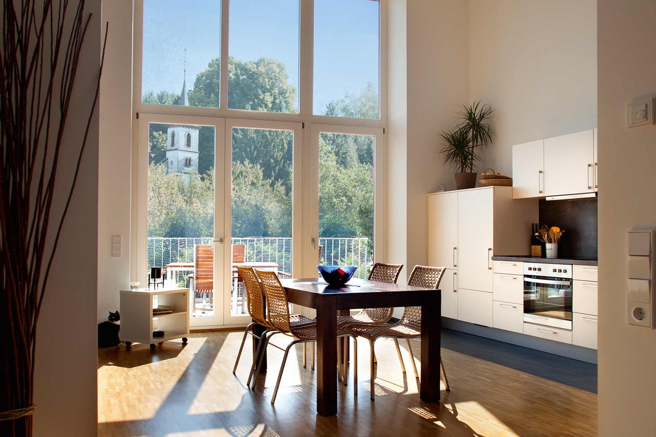 Salle à manger lumineuse avec table en bois, chaises, kitchenette et grande fenêtre