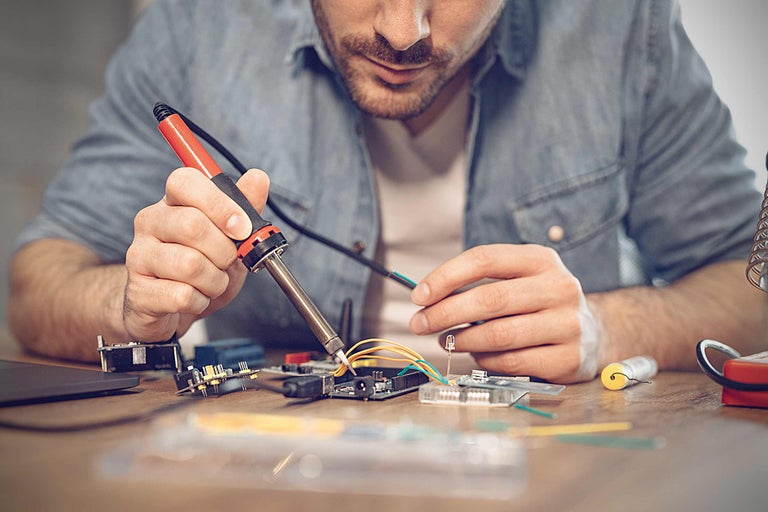 Un homme soude des composants électroniques avec un fer à souder sur un circuit imprimé.