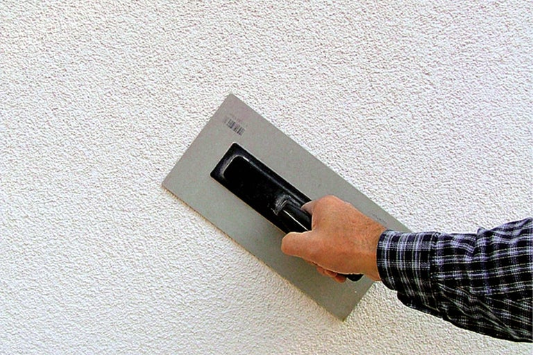Aussenwand mit Putzstruktur und Handwerker mit Glättkelle