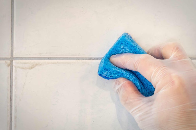 Nettoyage de carreaux avec une éponge par une personne portant des gants