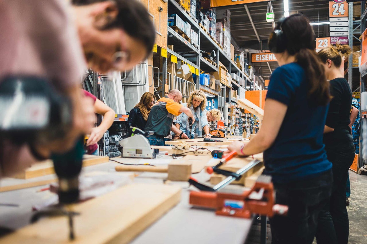 Personen arbeiten in einem Hornbach Baumarkt an einer Werkbank mit Werkzeugen.