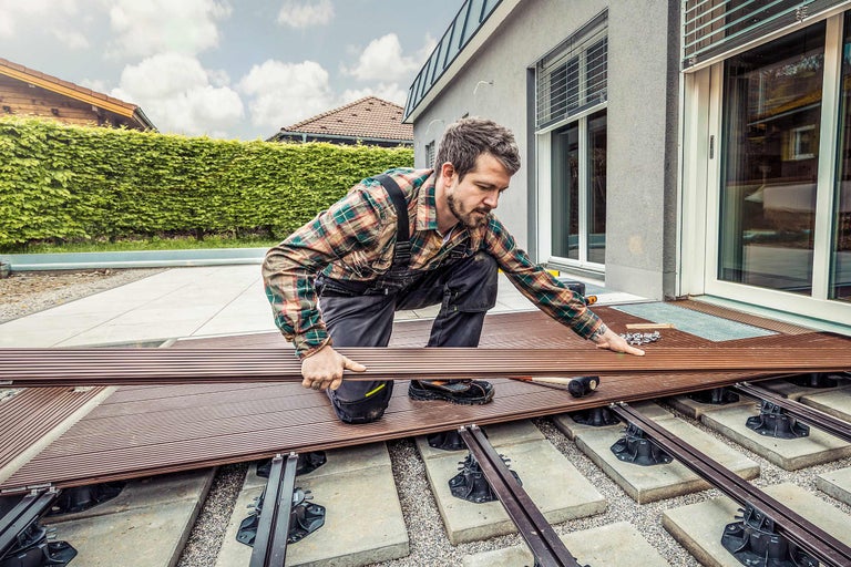 Un homme pose des lames de terrasse sur une terrasse avec des pieds réglables.