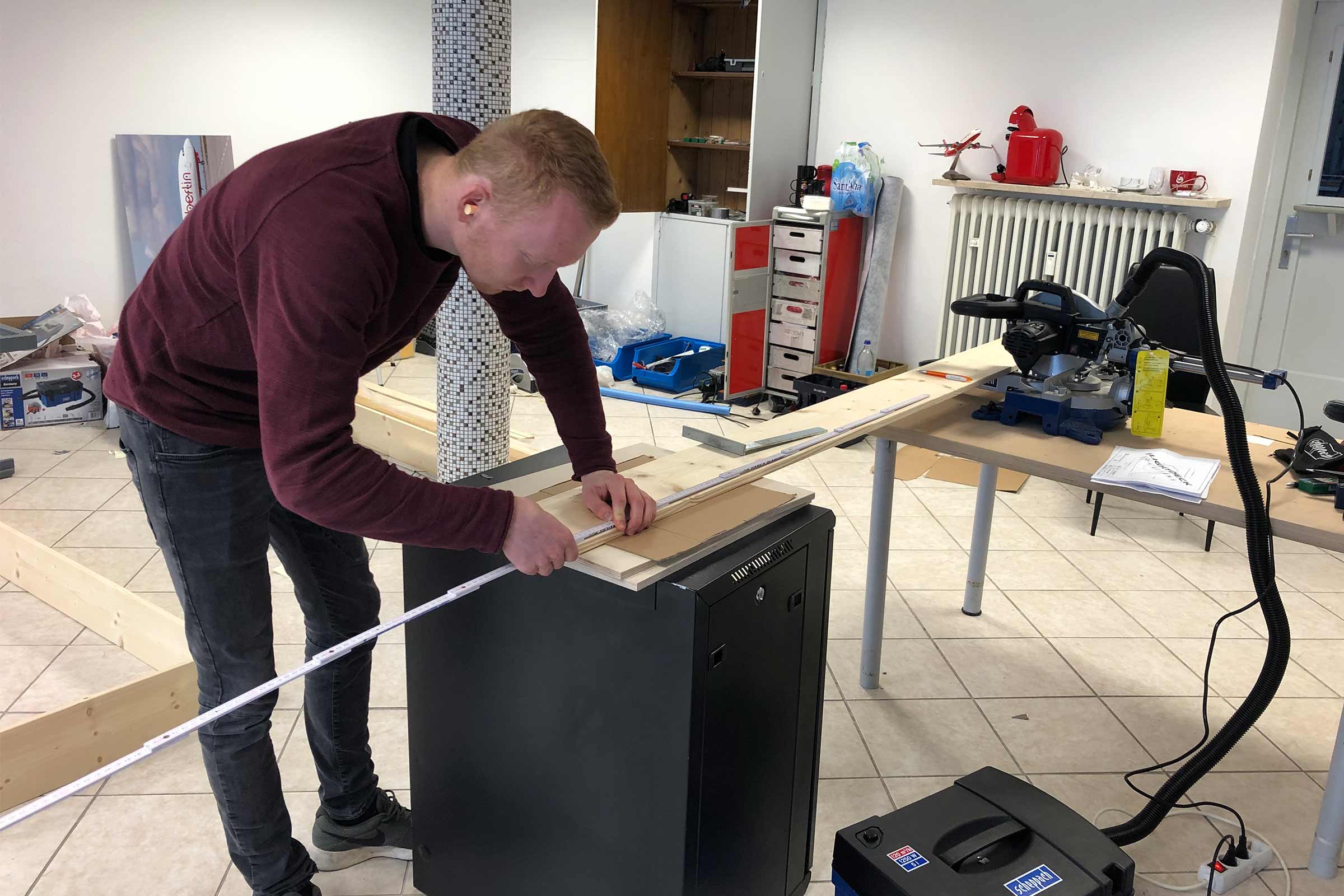 Un homme mesure une planche de bois avec un mètre pliant dans un atelier.