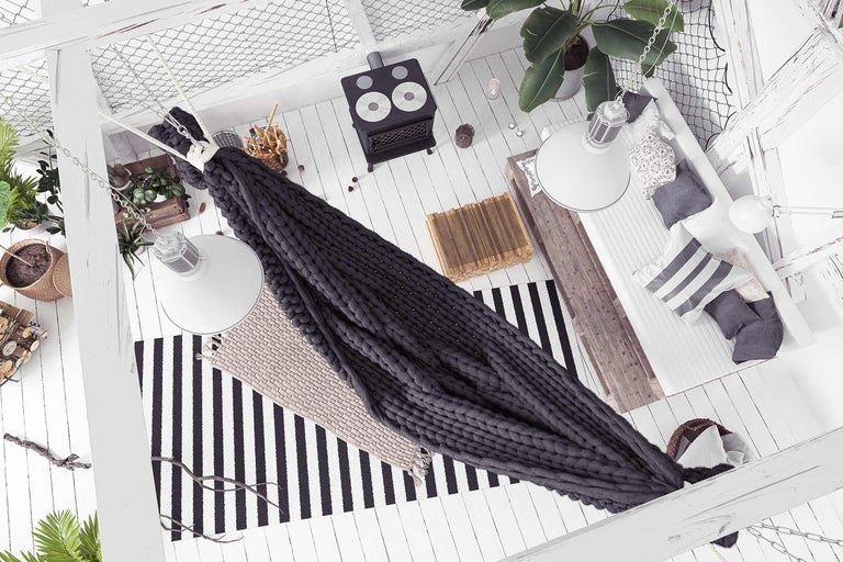 Vue intérieure avec fauteuil suspendu, poêle à bois, tapis, plantes et décorations.