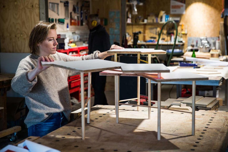 Femme dans un atelier arrangeant une structure en bois avec des plateaux et des pieds de table