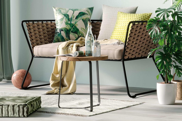 Scène de salon avec fauteuil en rotin, table ronde en bois, coussins et plante d'intérieur pour une ambiance chaleureuse