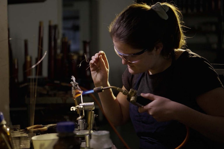 Femme avec lunettes de protection et lampe à souder travaillant le verre.