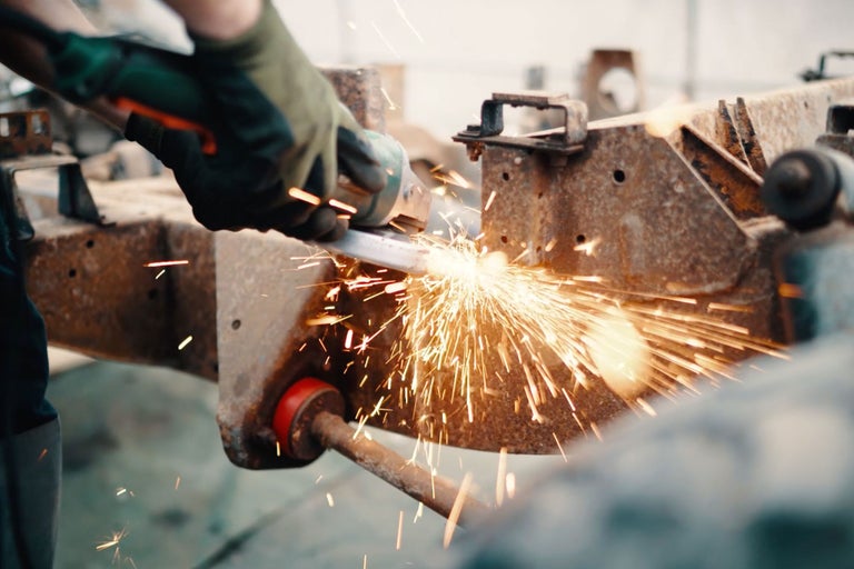 Une personne meule du métal avec une meuleuse d'angle, des étincelles jaillissent.