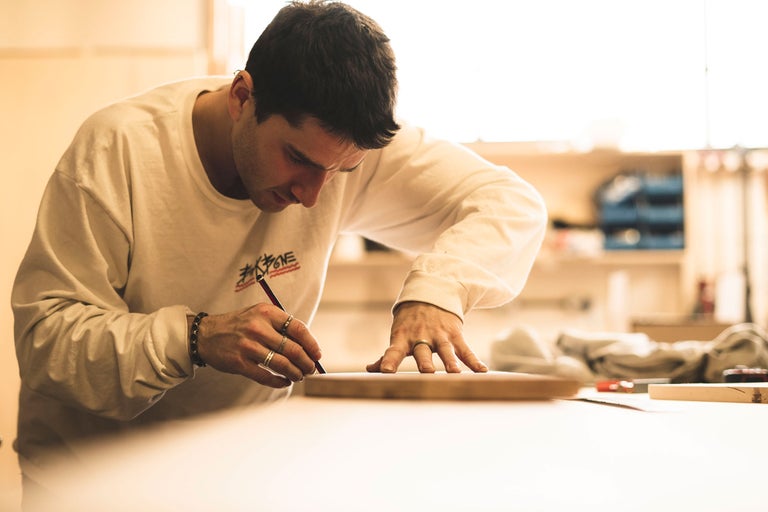 Un homme dessine avec un crayon sur une planche de bois.