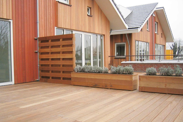 Terrasse en bois avec brise-vue et jardinières plantées devant une maison