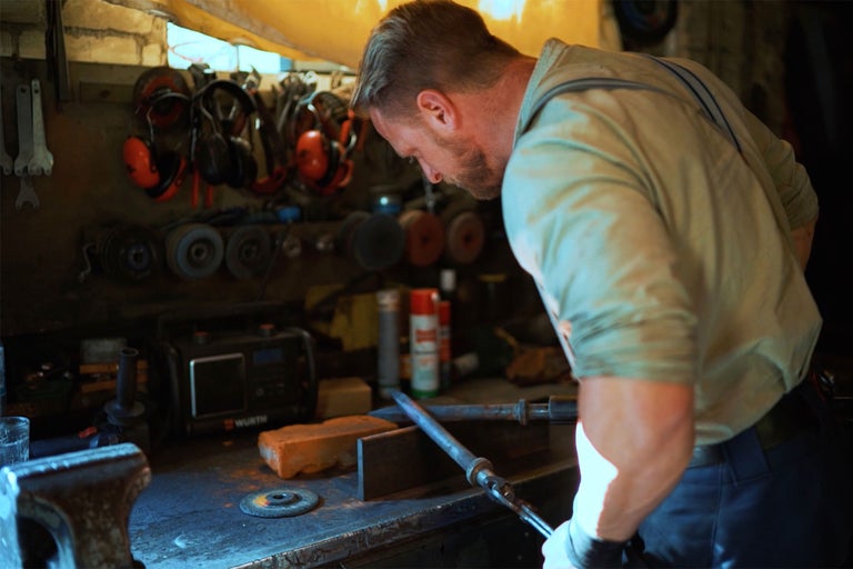 Ein Handwerker arbeitet in einer Werkstatt mit Werkzeugen wie Zangen, Schraubenschlüsseln und Schleifscheiben.