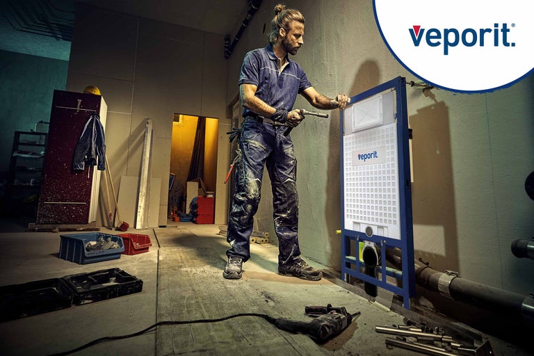 Un homme installe un bâti-support WC de la marque Veporit dans une construction brute.