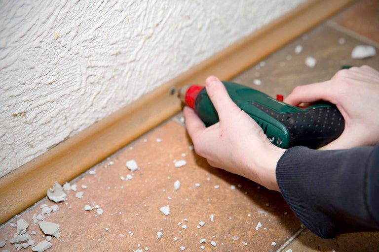 Un artisan fixe une plinthe en bois au mur à l'aide d'une visseuse sans fil