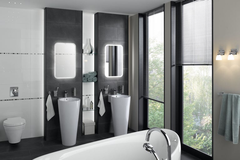 Helles Badezimmer mit zwei Säulenwaschbecken, beleuchteten Spiegeln und Badewanne